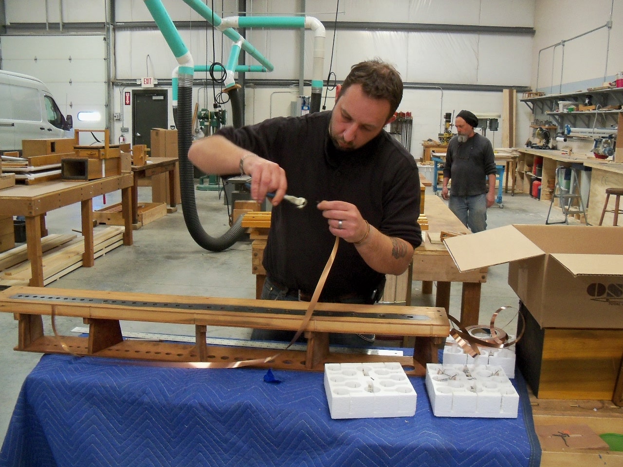 Photo of Voicer/Technician Sean Estanek installing copper strip to wind chest bottom board with Technician Joe Tillo in the background