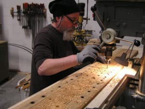 Technician using a drill press to drill holes in pipe organ wind chest bottom board
