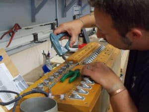 Sean Estanek connecting wire to each magnet on bottom board of pipe organ wind chest