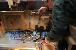 Organ Builder, James Leek examining electrical components inside pipe organ console and preparing for solid state components