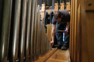 Technician Sean Estanek reinstalling cleaned & repaired pipes inside organ chamber