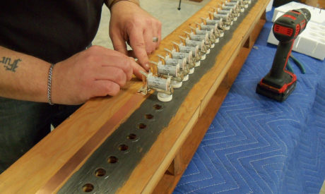 Technician Sean Estanek installing magnets to copper strip on bottom board of pipe organ wind chest.