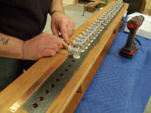 Technician Sean Estanek installing magnets to copper strip on bottom board of pipe organ wind chest.