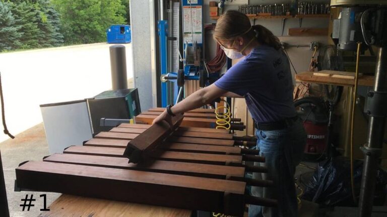 Technician Lifting a long wooden organ pipe from a row of matching pipes on a workbench.