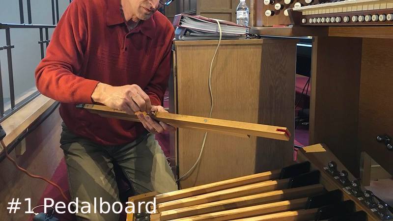 James holds and examines a long wooden key over a partially disassembled pipe organ pedalboard