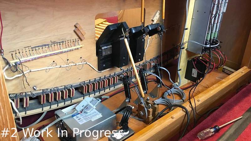 An open, interior view of a pipe organ console wooden housing showing wiring bundles, circuit components, contact pins, and leverage rods