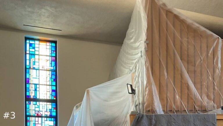 Close-up view of a graduated row of tall wooden organ pipes enclosed under clear protective plastic sheeting on an elevated platform