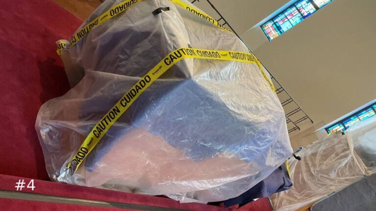 Close-up view of a graduated row of tall wooden organ pipes enclosed under clear protective plastic sheeting on an elevated platform