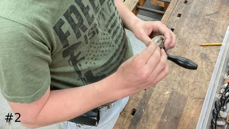 technician stands at a workbench holding and examining a small round hardware piece attached to a black wooden handle lever