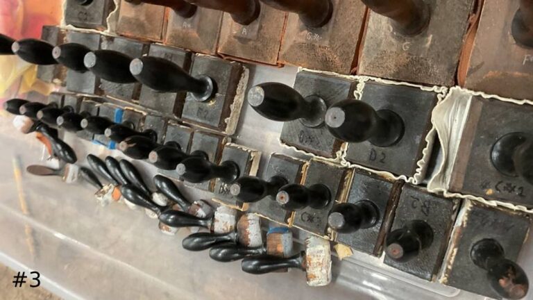 An angled close-up view of a large collection of weathered wooden organ pipe stoppers fitted with black vertical handles