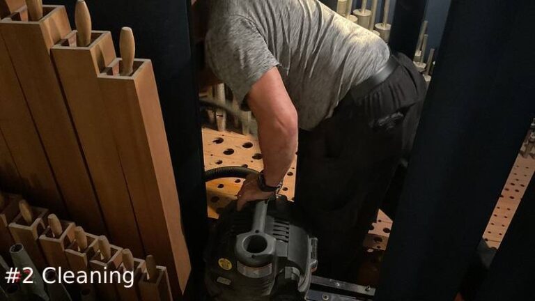 An organ technician uses a utility vacuum to clean out a wooden toeboard framework