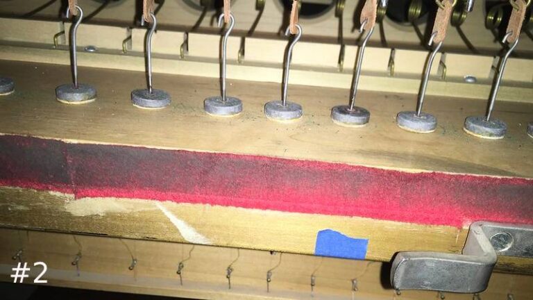 Close-up of a wooden pipe organ mechanism showing a neat row of small metal vertical wires ending in round leather discs.