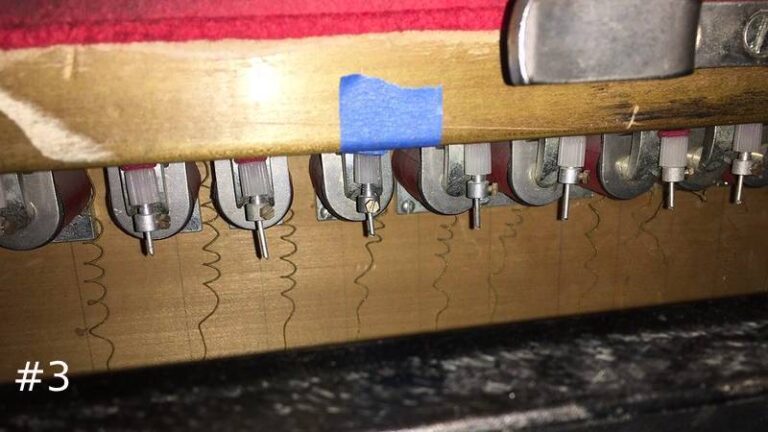 Close-up of a pipe organ wooden rail showing a row of newly mounted metal electromechanical valve switches with small wire pins.