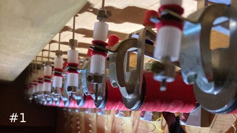 Close-up view looking down a long, repeating row of electromechanical pipe organ valve magnets with red coils and white plastic fittings.
