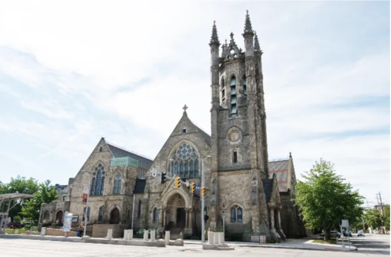 A historic gothic revival stone church with a tall decorative bell tower, and detailed arched windows.