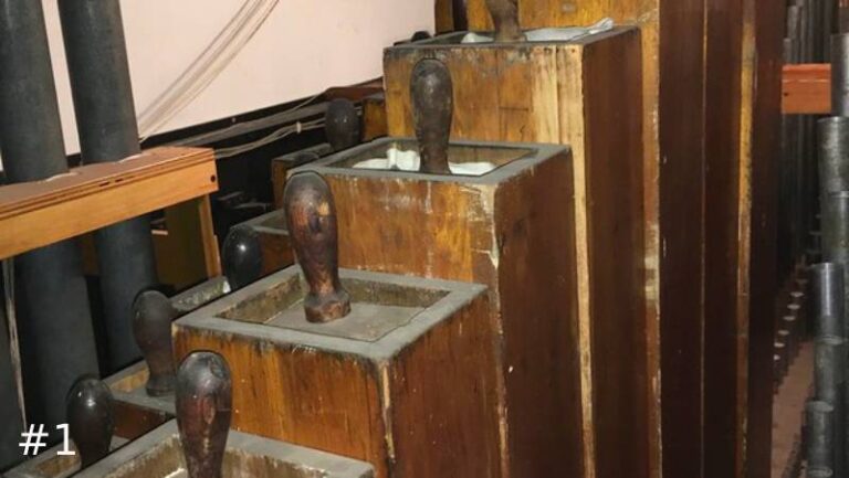 Close-up of a graduated row of old, dusty wooden organ pipes with vertical wooden handles sticking out of their top stoppers