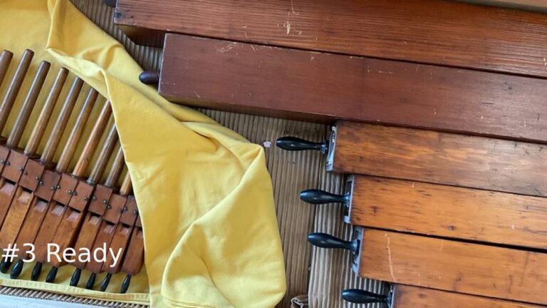 Top-down view of cleaned and polished square wooden organ pipes with black stopper handles, resting next to a row of small wooden pipe components