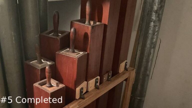 restored square wooden organ pipes with upright handles stands fully assembled inside an organ chamber, secured by a wooden rack framework
