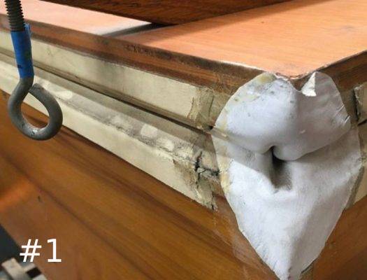Close-up of a damaged, cracking white leather corner gusset on a layered wooden pipe organ bellows assembly.