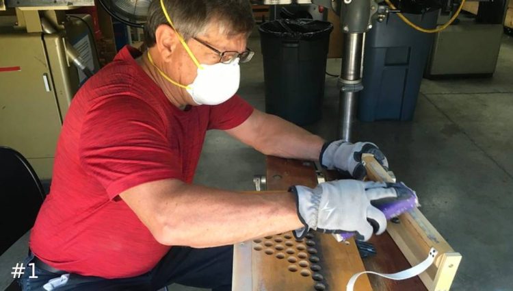 A Leek Pipe Organ Company technician working with gloves uses a sanding block to smooth a wooden component on a workshop table.